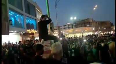 Iran: a woman sits on a utility box and cuts her hair in Kerman to protest Masha Amini's murder. Protesters chant, "Death to the dictator."