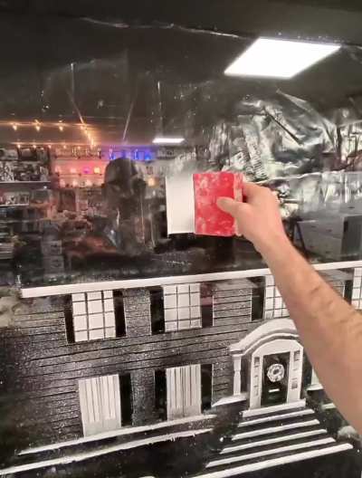 spray-snow artist creating Home Alone on a window (@snow.graffiti.scott)