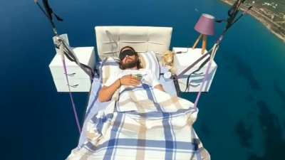 Man on bed suspended by parachutes flies away and takes a nap