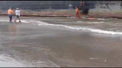 Man throws life preserver ring to another man clinging from the steps on a ship.