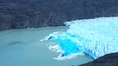 Glacial iceberg shifts revealing the deep blue of older, compressed ice