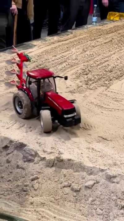 A remote control tractor tilling a small field.