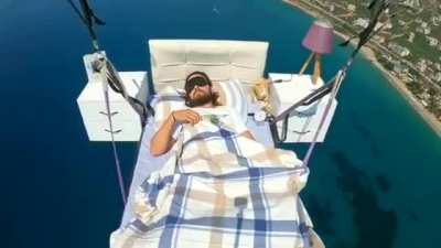 Man on bed suspended by parachute flies away and takes nap